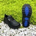 Boys' black lace-up school shoes photographed on white gravel with the tread sole showing