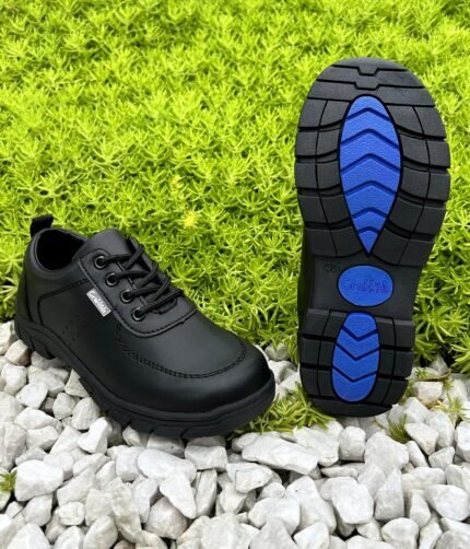 Boys' black lace-up school shoes photographed on white gravel with the tread sole showing