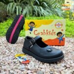 Girls' black buckle school shoes displayed on gravel beside the shoe box