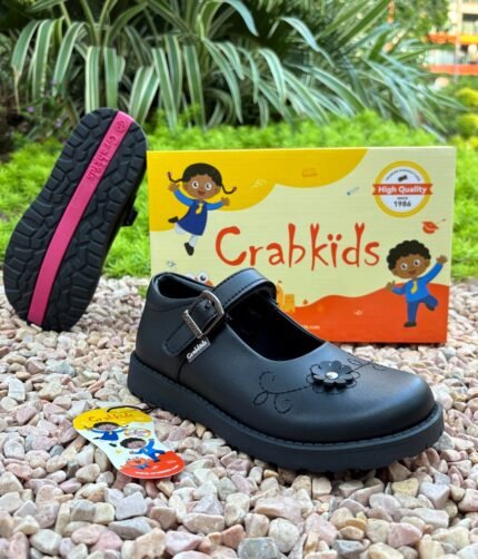 Girls' black buckle school shoes displayed on gravel beside the shoe box