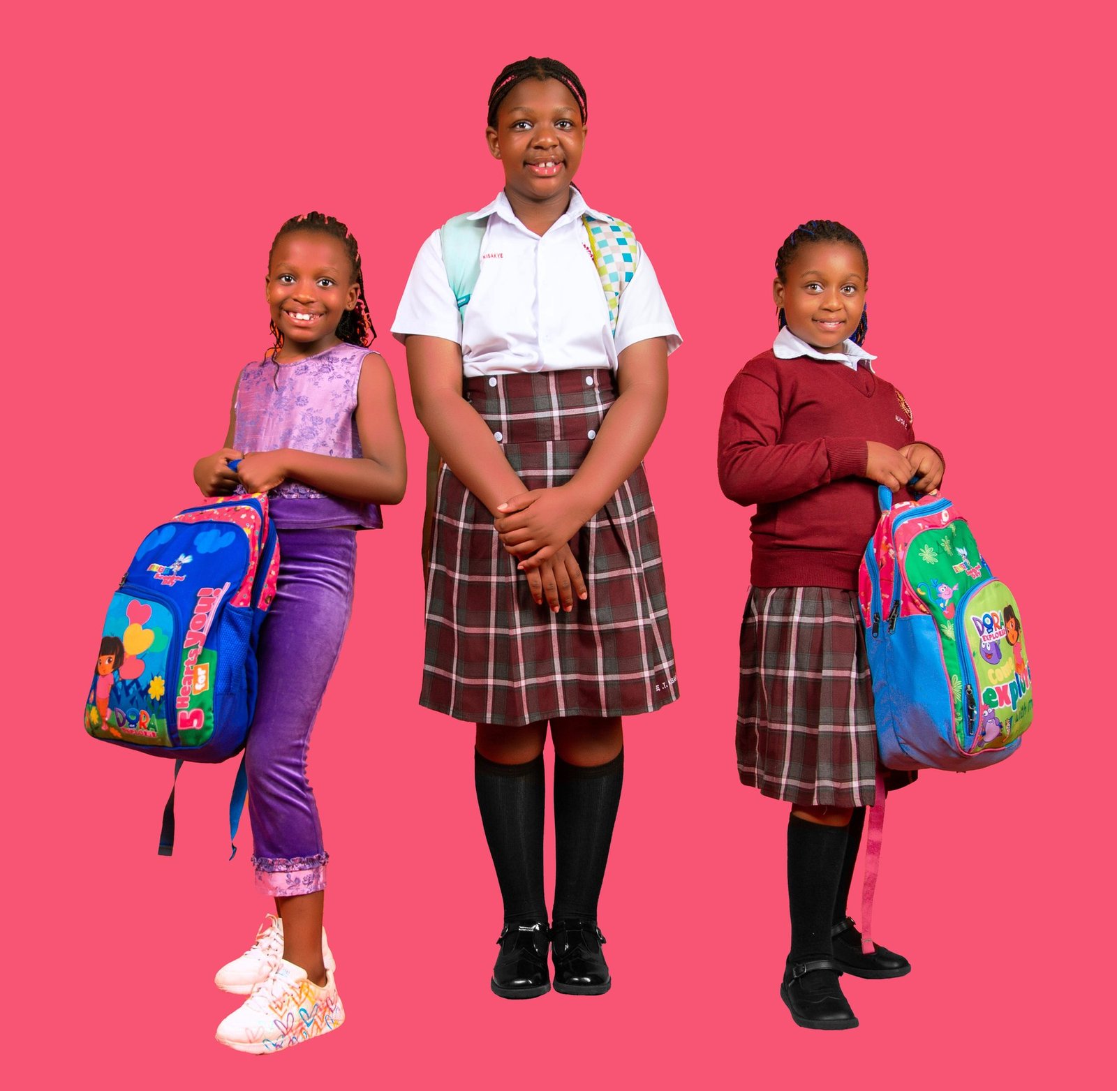 Three Ugandan schoolgirls in uniform holding colourful Kicks and Packs backpacks